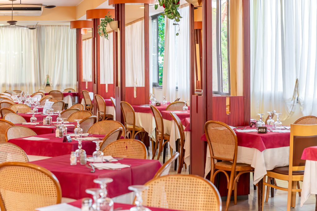 Interno di un ristorante elegante con tavoli apparecchiati e sedie di legno intrecciato.
