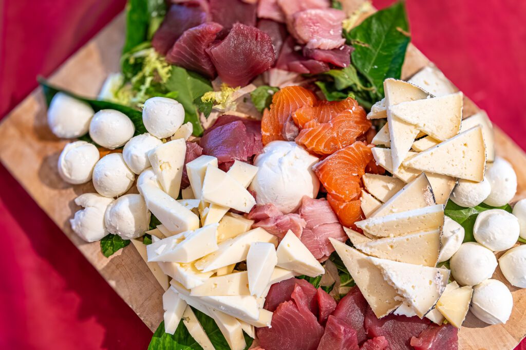 Tagliere di formaggi e affettati misti con mozzarella e salmone su sfondo rosso.