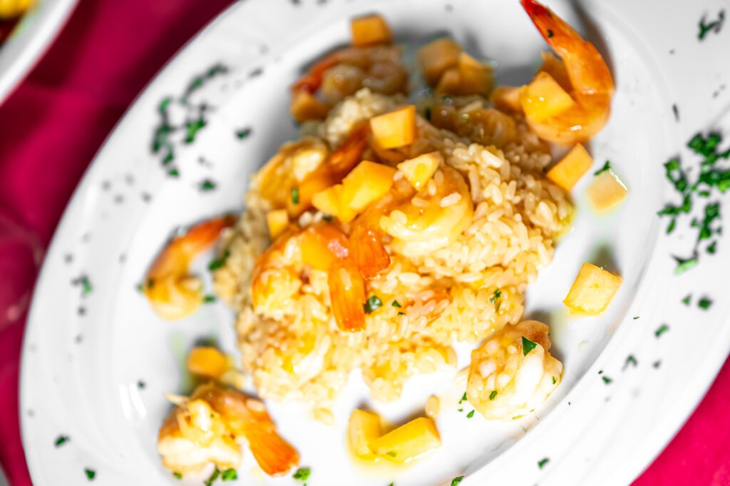 Piatto di risotto con gamberetti e cubetti di frutta su fondo rosso.