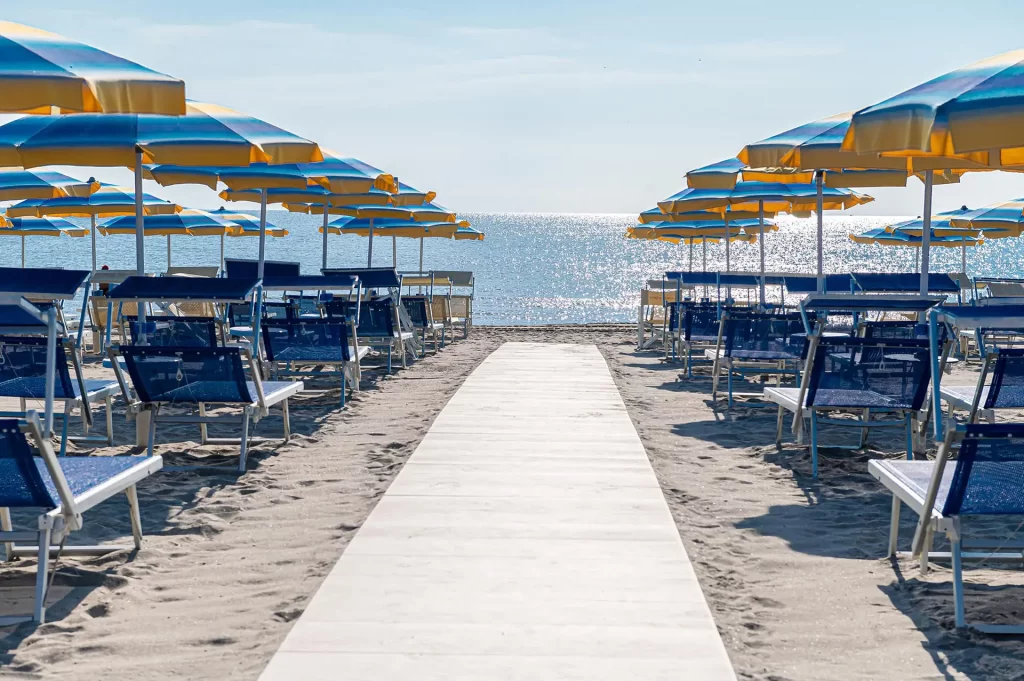 Spiaggia con lettini blu e ombrelloni giallo-blu, vista verso il mare.