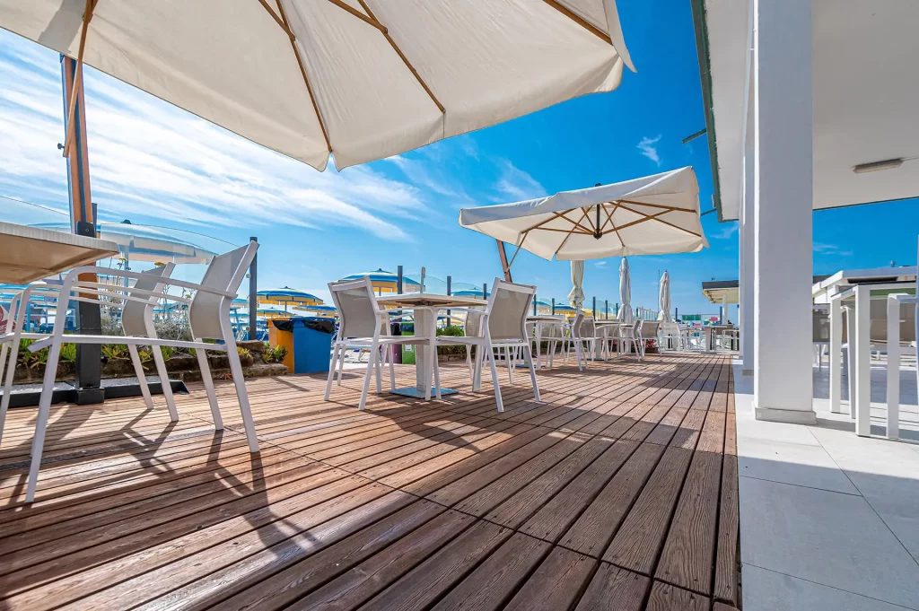 Terrazza soleggiata con tavoli e ombrelloni vicino a una spiaggia.