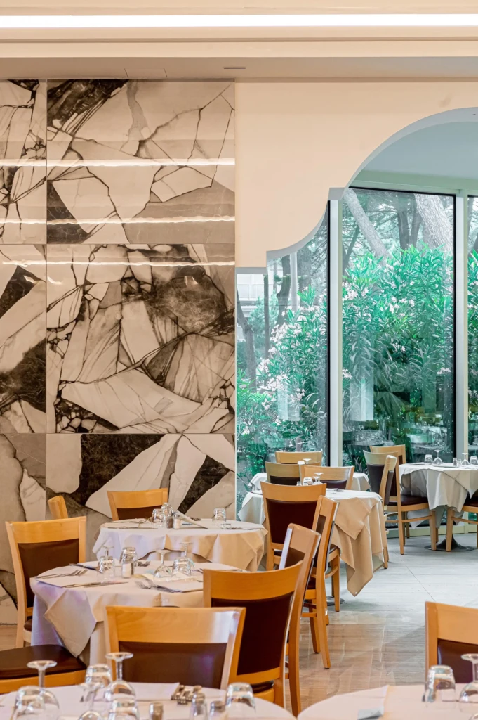 Sala di un ristorante elegante con tavoli apparecchiati e vista sul giardino attraverso grandi finestre.