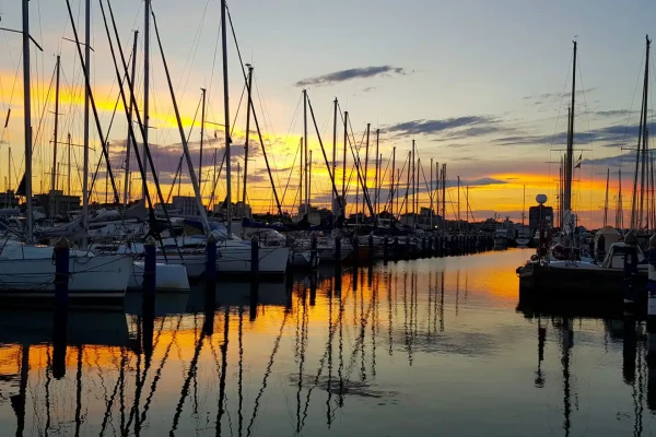 Tramonto su un porto con riflessi colorati tra le barche a vela.