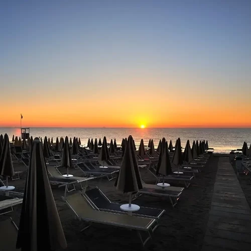 Tramonto su una spiaggia con file di lettini e ombrelloni chiusi.