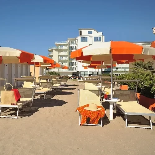 Spiaggia attrezzata con ombrelloni e lettini, sfondo di edifici moderni.