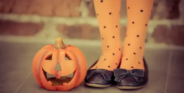 Calzini arancioni a pois e zucca intagliata di Halloween accanto a scarpe nere.